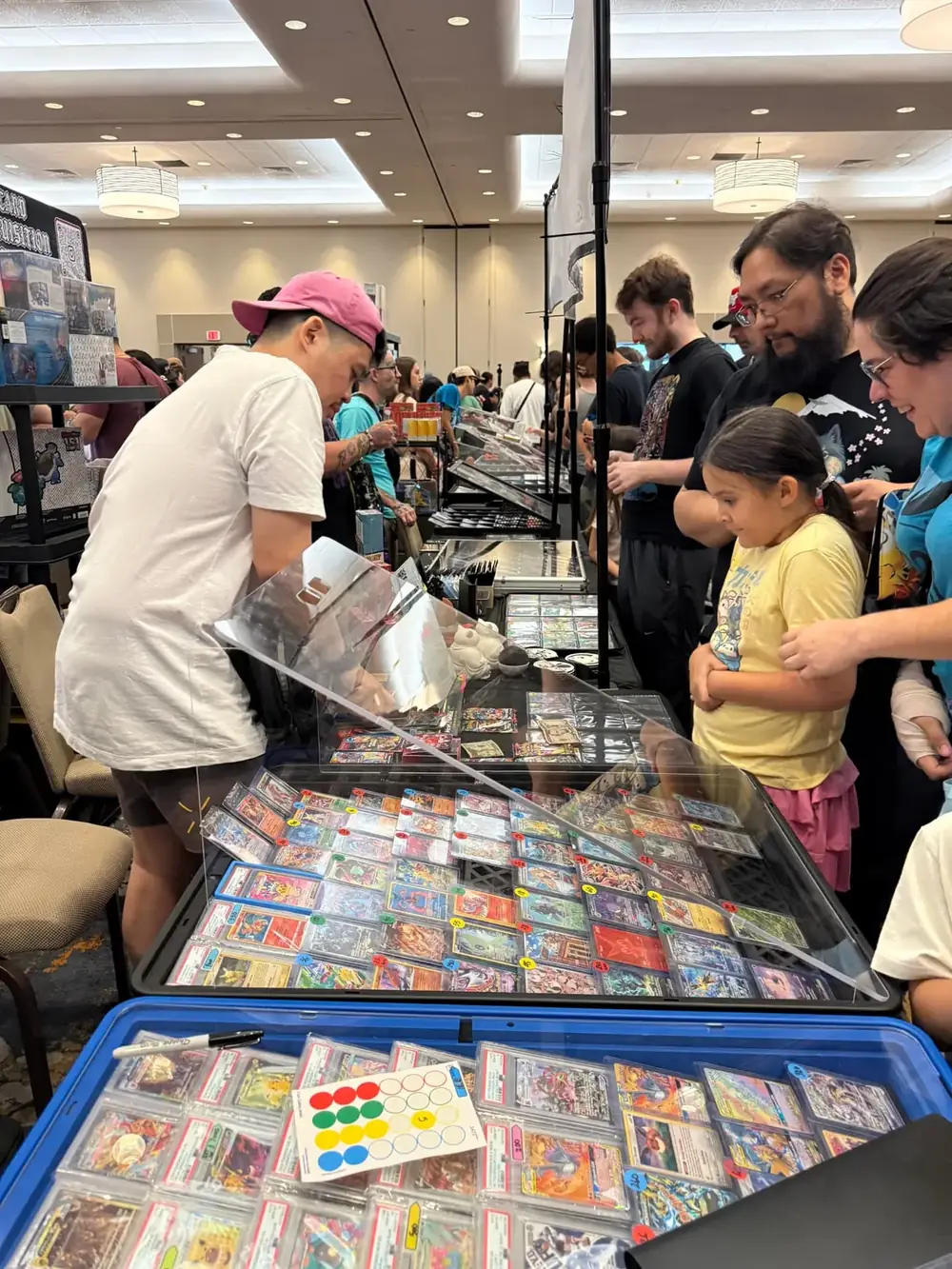Crowd of collectors around glass cases of Pokémon singles and slabs at The Cactus TCG Show in Mesa, Arizona