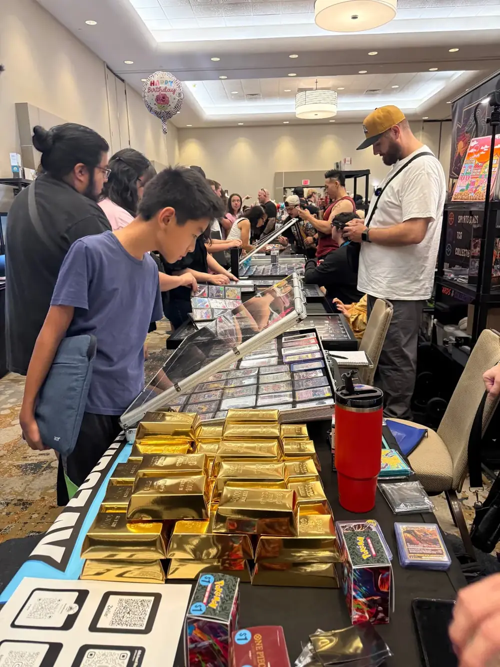 Vendor table stacked with gold mystery boxes and graded Pokémon slabs at The Cactus TCG Show in Arizona